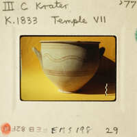 A clay pot with decorative lines on its surface, photographed against a yellow background.