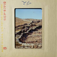 A photograph of an ancient stone wall with people walking along it, set against a clear sky and dry landscape.