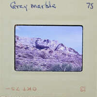 A vintage photograph of a rocky mountain landscape with a film strip label reading "Grey Marble" and number 75.
