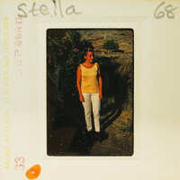 A woman standing outdoors, possibly on a farm or rural area, with a vintage Polaroid photo aesthetic.