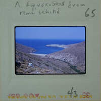 A vintage photograph of a coastal landscape with blue water and rocky hillsides, possibly from Greece.
