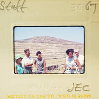 A group of people standing on a hillside with a mountainous landscape behind them, captured in an old-fashioned photo format.