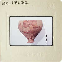 Ancient vase with intricate designs and missing pieces, photographed on a white surface.