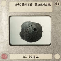 An old, black incense burner with holes on a card.