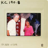 The image shows an older man and woman standing next to each other, with the man looking at something off-camera while the woman looks directly at him. Catalog number KC.190.8