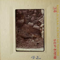 This is a photograph of an old slide depicting a rocky, earth-toned landscape with a small figure in the foreground.