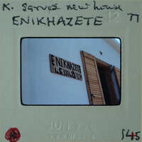 The image shows a photograph of a building with a sign that reads "ENNIHZAKEITE", which is placed on a film strip labeled with the date "JUNE 12 77" and has handwritten notes on it