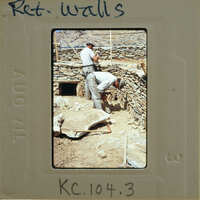 Two men working on a stone wall with tools.