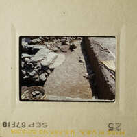 A photograph of an archaeological site with stone ruins, dirt path, and rocky terrain.