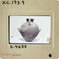 Ancient vase with visible cracks and wear, photographed on a white surface.
