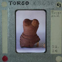A small, damaged clay figurine on a white surface with a film strip border and annotations.