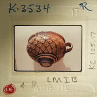 Photo of a clay pot with intricate designs, displayed on a paper with handwritten notes and dates.