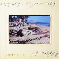 A photograph depicting an archeological site with ruins and a rocky beach, taken from a high angle perspective.