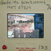 A photograph of a closed gate with a sign and a house in the background, on an old-fashioned film strip.