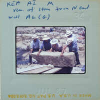 Four men working on a large stone block at an archaeological site.
