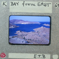 A photograph of a coastal landscape with mountains and water, enclosed within a film strip frame.