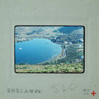 A vintage photograph of a scenic lake with boats and houses on the shore, framed by mountains.