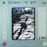 A photograph of a stone drainage ditch with a film strip border.