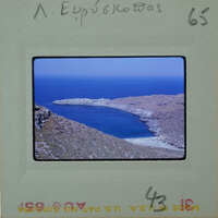 A photograph of a scenic coastal landscape with blue water and rocky terrain, possibly from an old film negative.