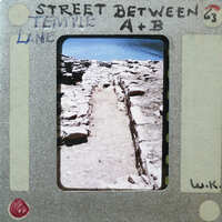 A vintage photograph of a stone walkway leading to the sea, with handwritten notes on its border.