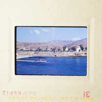 A scenic view of a beach and ocean with boats, captured on an old photo slide.