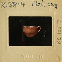 Ancient ceramic cup on display with visible cracks and chips.