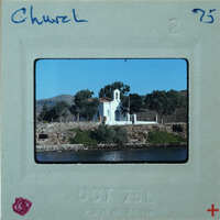 Small church on the water, with mountains and trees in the background.