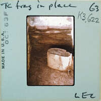 Broken base of terracotta figurine skirt on dirt floor surrounded by stone walls.