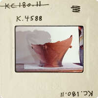 Old clay pot on display with visible damage and shadow cast on wall.