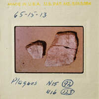 Photograph of two broken pieces of pottery on a surface, with handwritten notes and numbers indicating its identification.