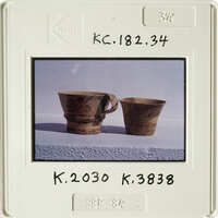 Two clay cups with designs on a white surface.