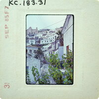 A vintage photograph of a quaint village with white buildings and lush greenery, enclosed within an old film strip frame.