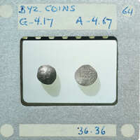 Two old coins displayed on a white stand with labels and numbers written on it.