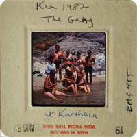 A group of people posing together on a beach, with some standing and others sitting in shallow water.