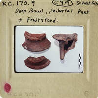 Three ancient clay objects, possibly pottery shards, on display with labels and numbers indicating their identification.