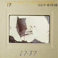 The image shows an old photograph with a black and white scene, possibly from an archaeological site, featuring broken stone structures.