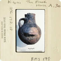 Ancient pottery with a face-like design, displayed on a white background.