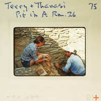 Two people working on a stone wall with bricks and mortar.