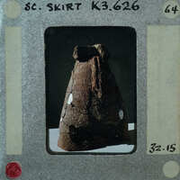 The image shows a vintage Polaroid photo of an artifact, which appears to be a pottery item with a handle and possibly some engravings or markings on its surface. The photograph is placed within the confines of a white Polaroid frame that