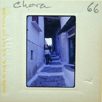 A vintage photo of a narrow stone street with people walking and buildings on either side.