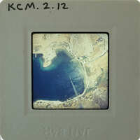 Aerial photo of a coastal area with water and land features, mounted on a label with a border.