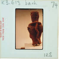 Clay figurine from behind, displayed with a white background and a label.