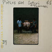 Two men standing next to a large clay pot.