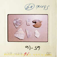 The photograph shows a collection of small, irregularly shaped pieces of pottery displayed on a light background.