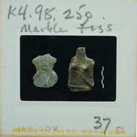 A small clay figurine of a humanoid shape on display with a price tag and description.
