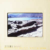 This is an image of a stone structure, possibly ruins, near a body of water with a clear sky above.