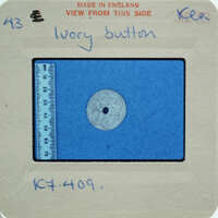 A close-up image of a button on a measuring tape, with labels and measurements indicating its size.