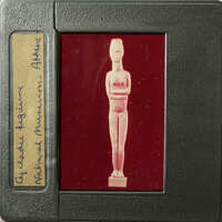 Ancient Egyptian artifact, possibly a figurine or amulet, displayed on a red background with labels and markings.