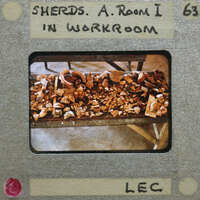 Old slide with a label and an image of a workbench with pottery shards on it.