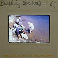 A group of men working on a sea wall at the water's edge.